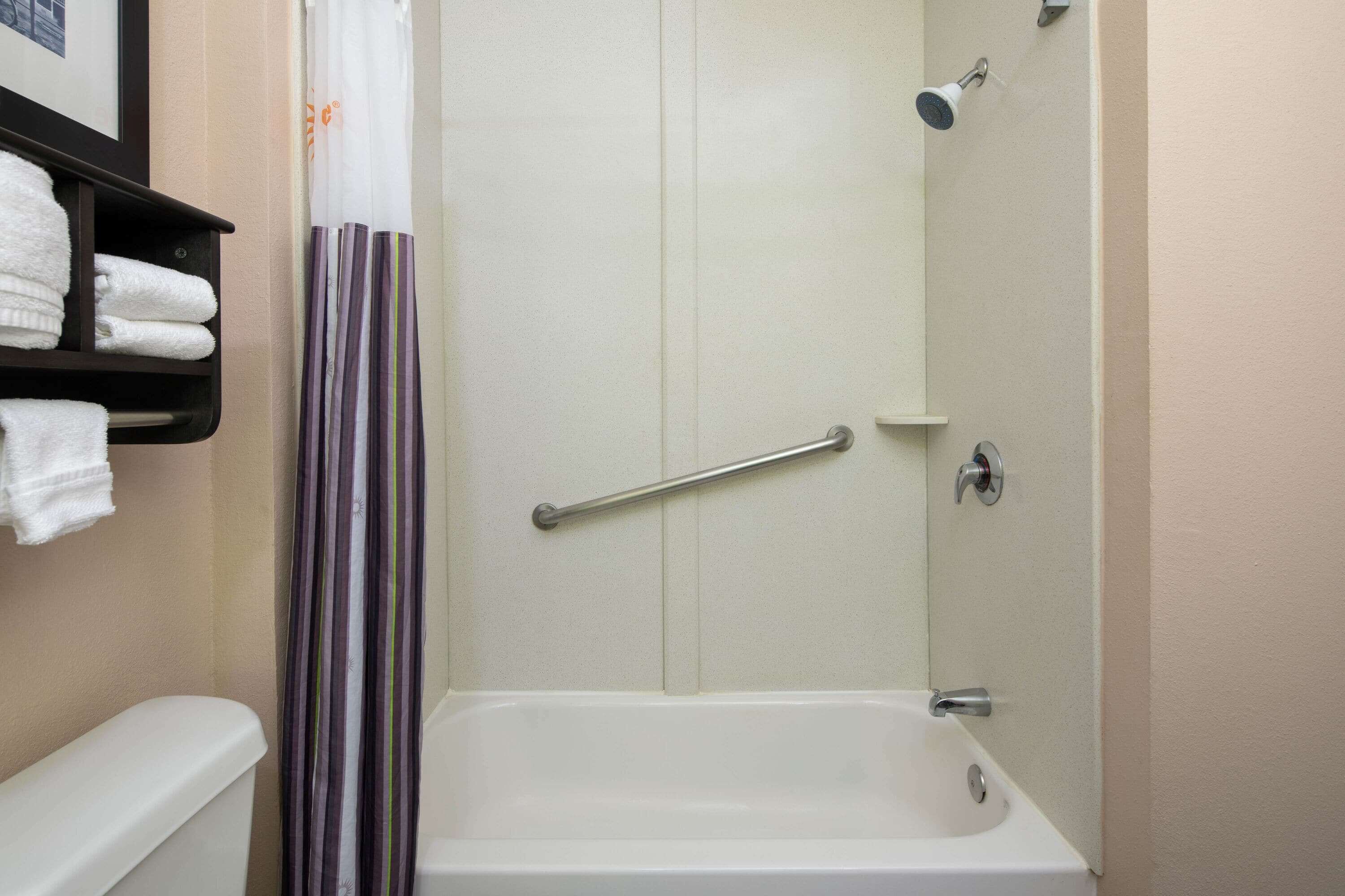 A bathroom with a bathtub, a shower, a handrail, and a towel rack with towels.