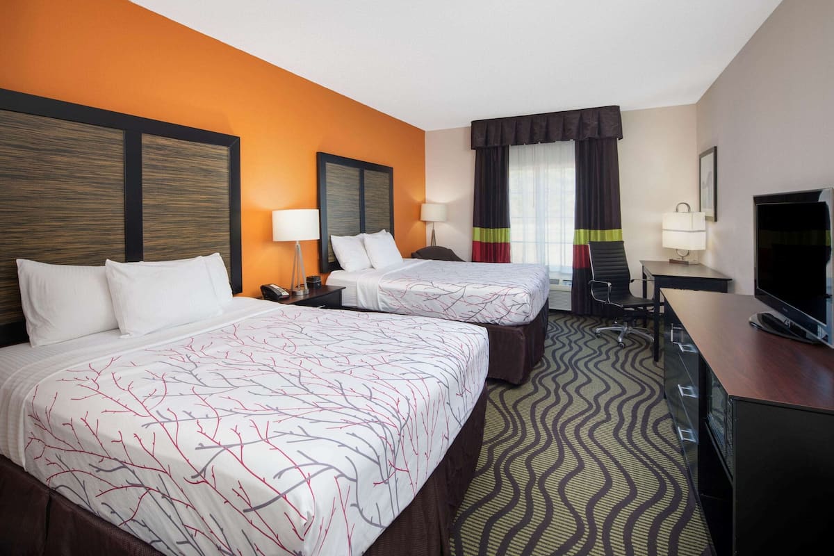 A hotel room with two beds, a desk, a television, and a patterned carpet.