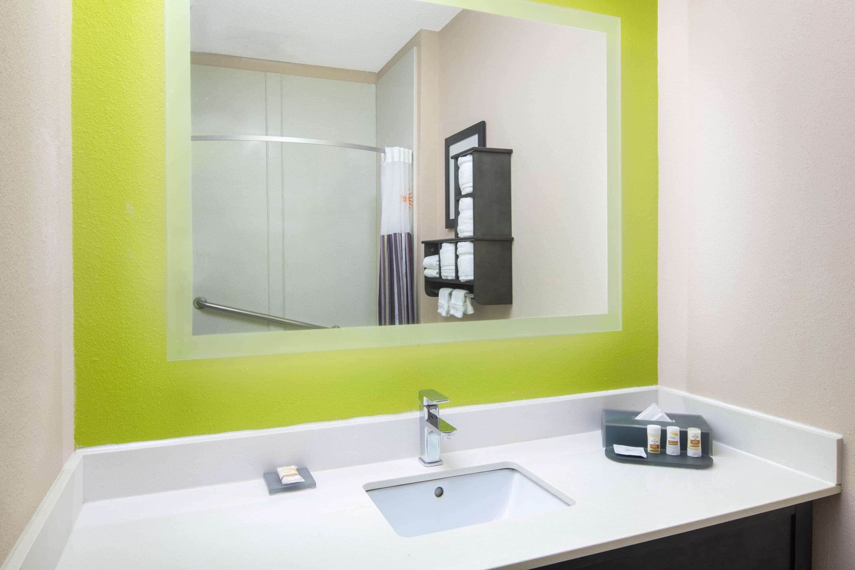 Un baño de hotel con un espejo grande, un lavamanos y un perchero para toallas.