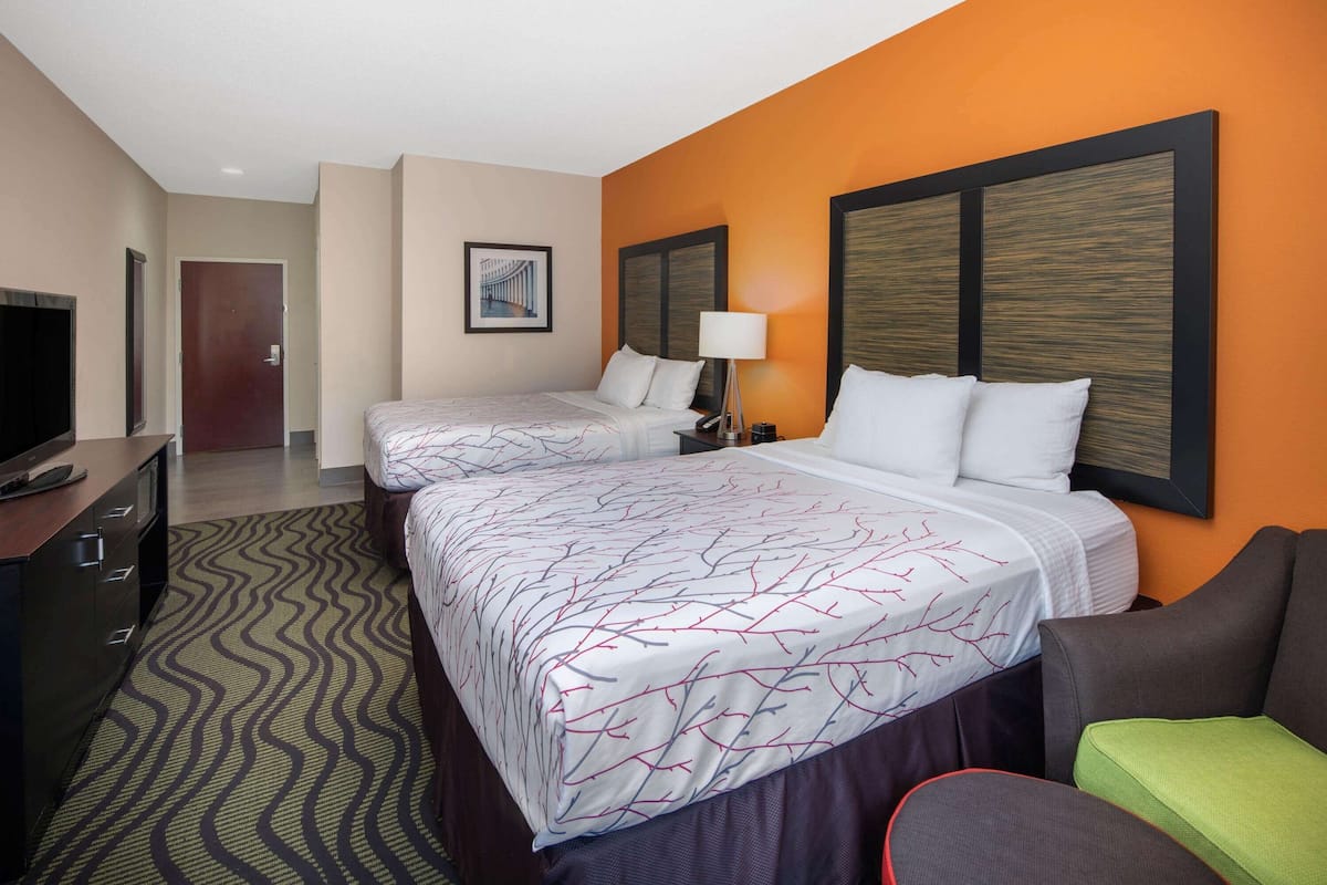 A hotel room with two beds, a TV, a desk, and a patterned carpet.