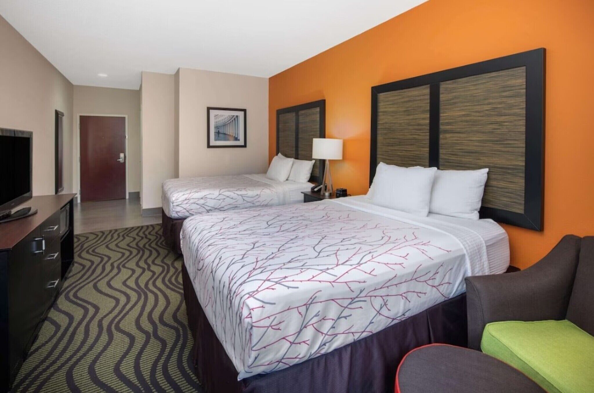 Habitación de hotel con dos camas, televisión, escritorio y alfombra estampada.