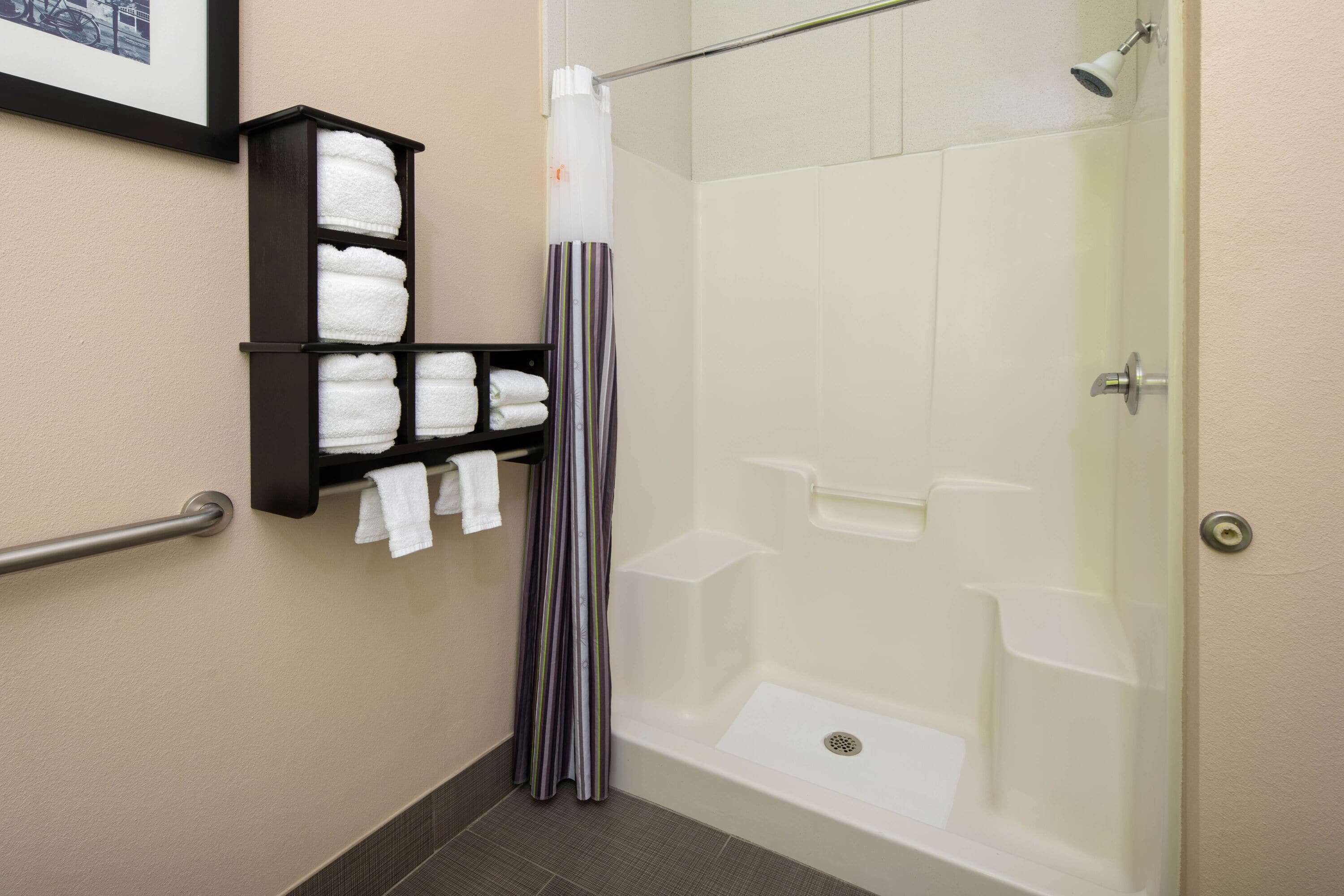 A shower with a glass door, a towel rack with folded towels, and a striped shower curtain.