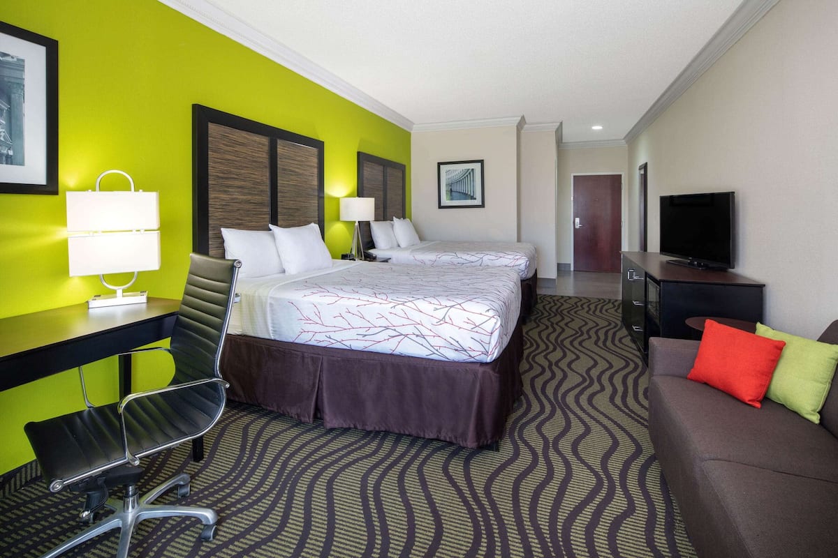 A hotel room with a bed, a desk, a chair, a TV, and a sofa.