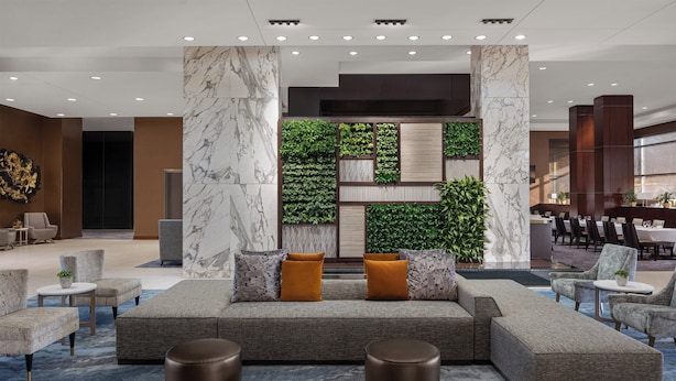 A modern lobby with a sectional sofa, round ottomans, and a green vertical garden wall.