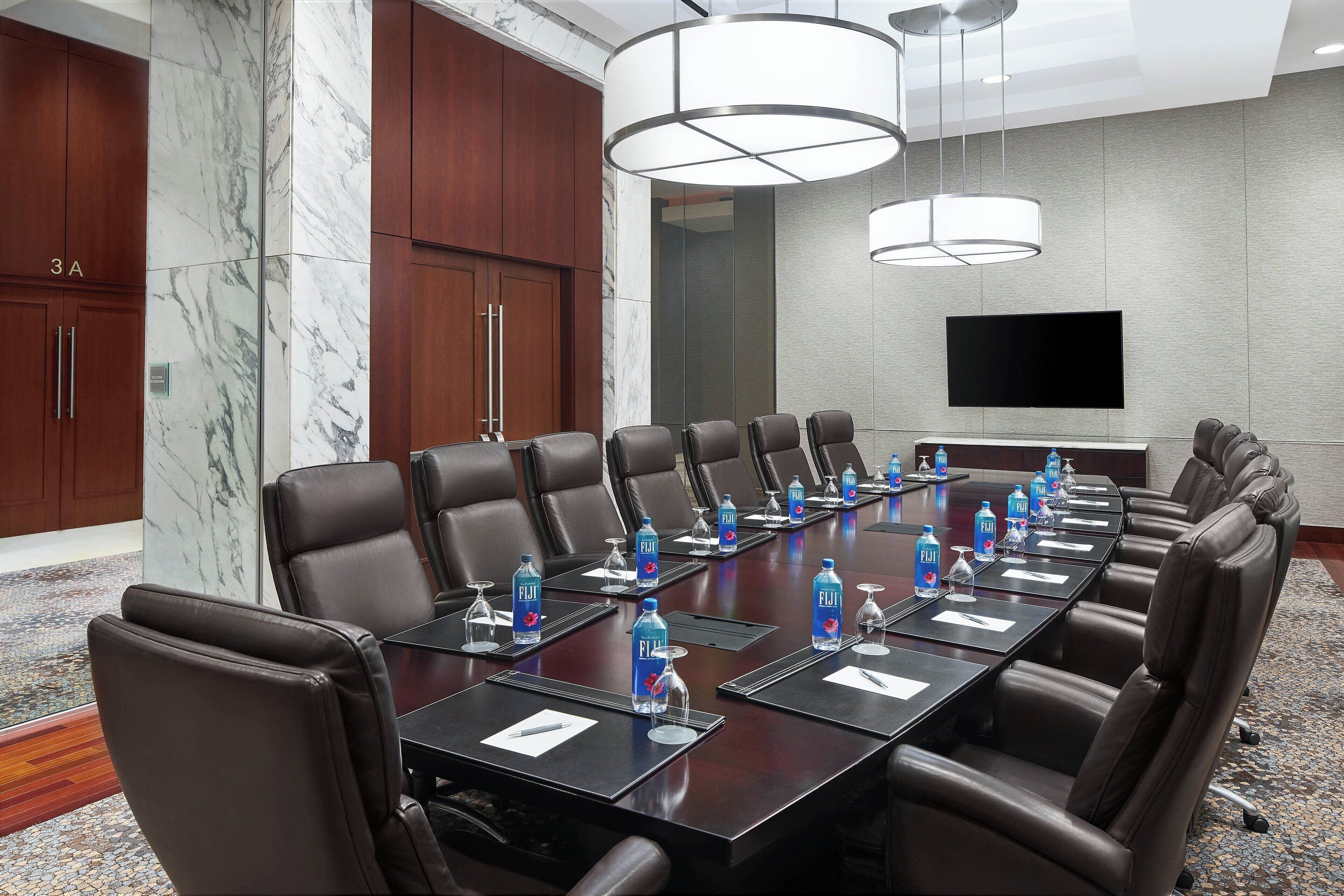 A conference room with a long table, multiple chairs, water bottles, and a television screen.