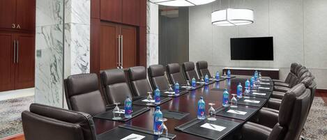 A conference room with a long table, multiple chairs, water bottles, and a television screen.