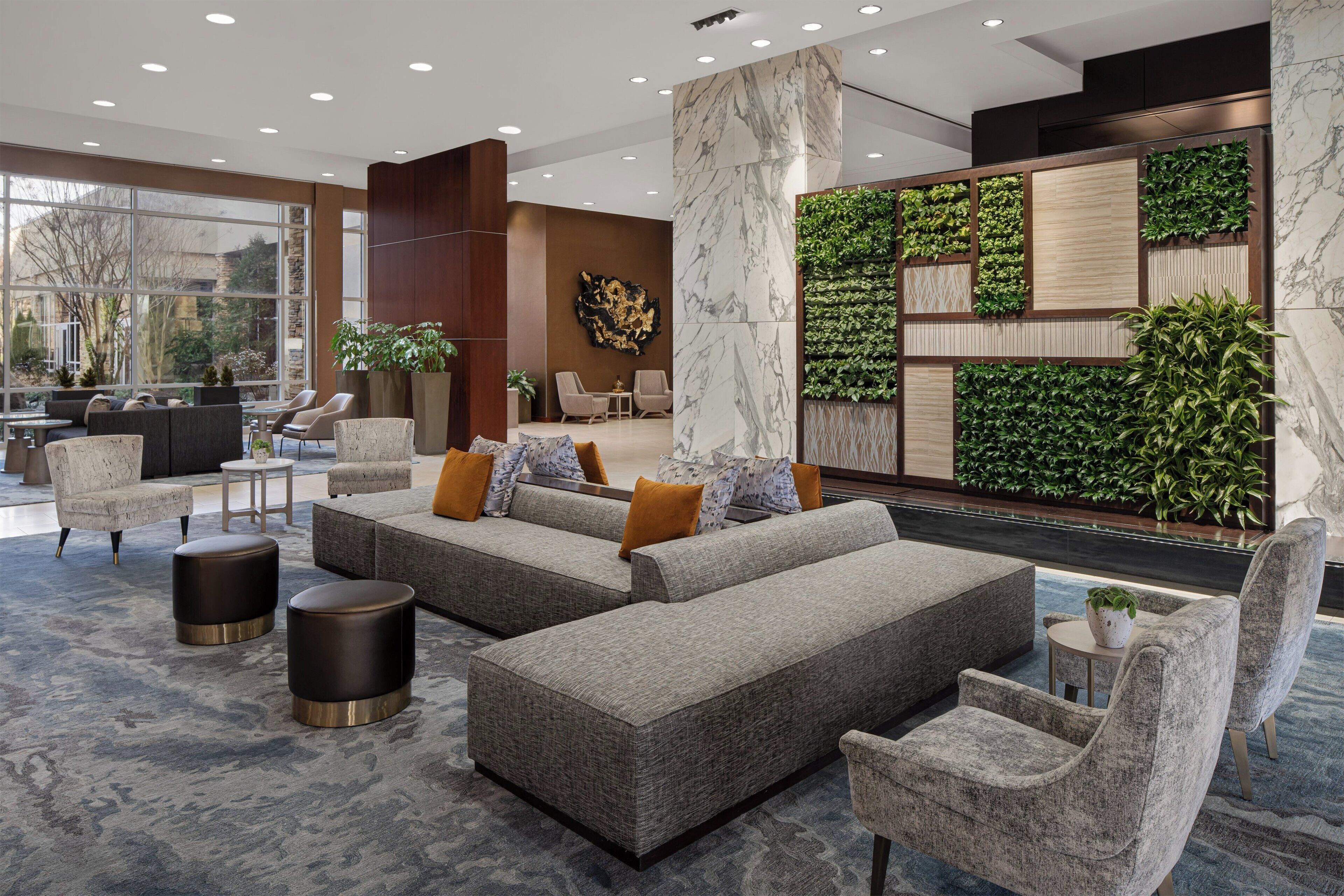 Eine moderne Lobby mit Ecksofas, Sessel und einer großen Grünwand.