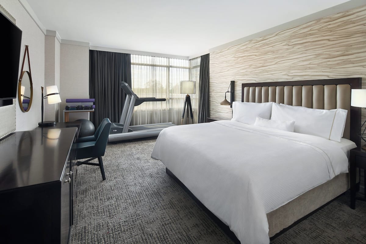 A hotel room with a large bed, a desk with a chair, a treadmill, and a TV.