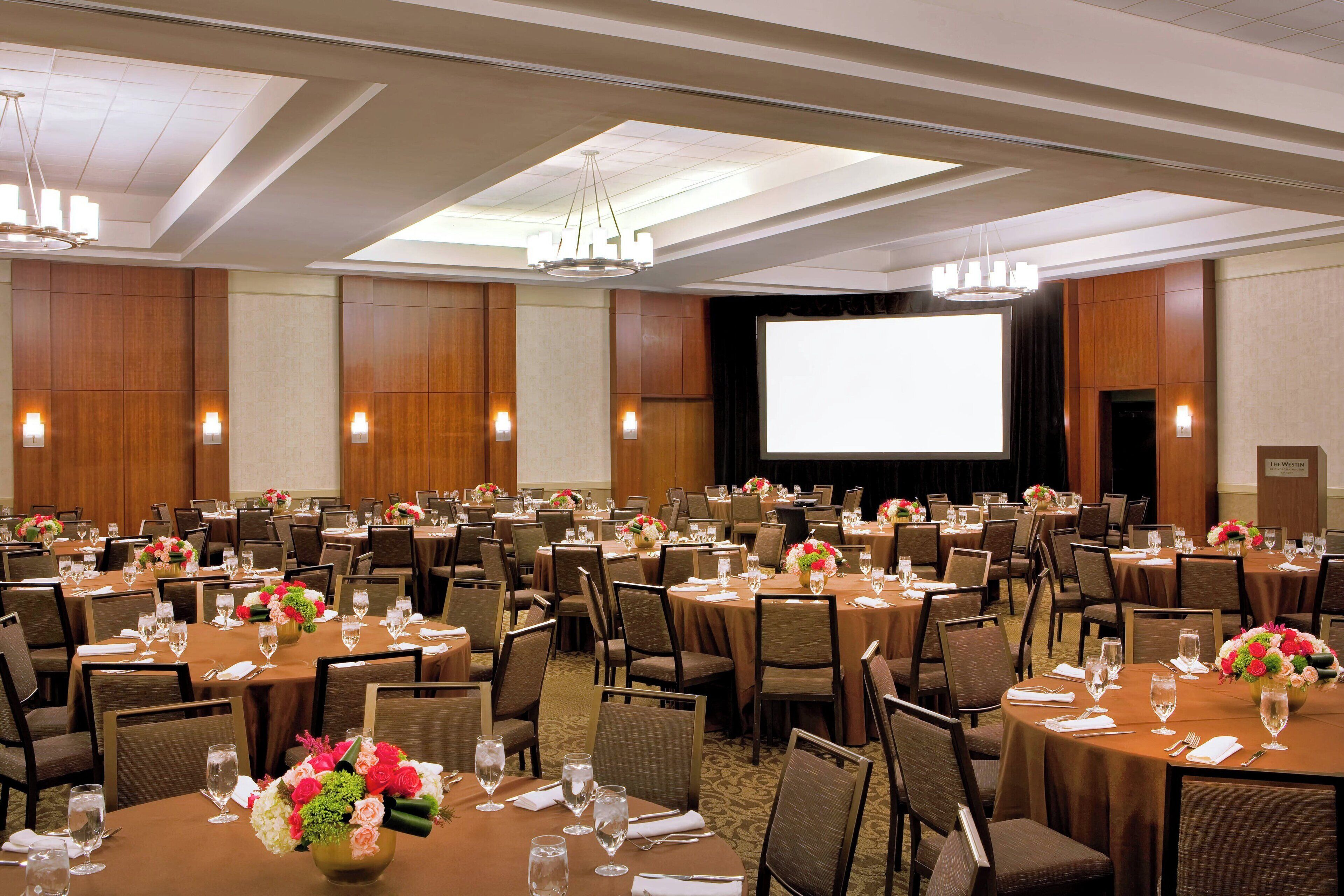 A large conference room with multiple tables, chairs, and a projection screen.