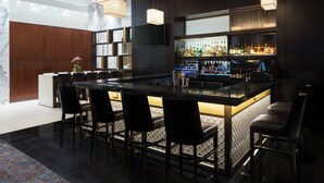A modern bar area with a marble countertop, black bar stools, and a well-stocked liquor shelf.