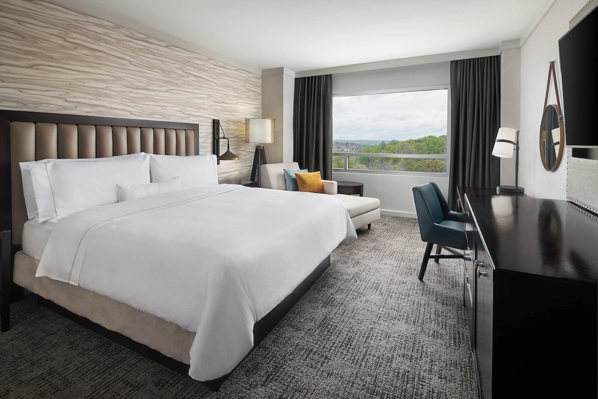 A hotel room with a large bed, a desk, a chair, and a view of the outdoors.