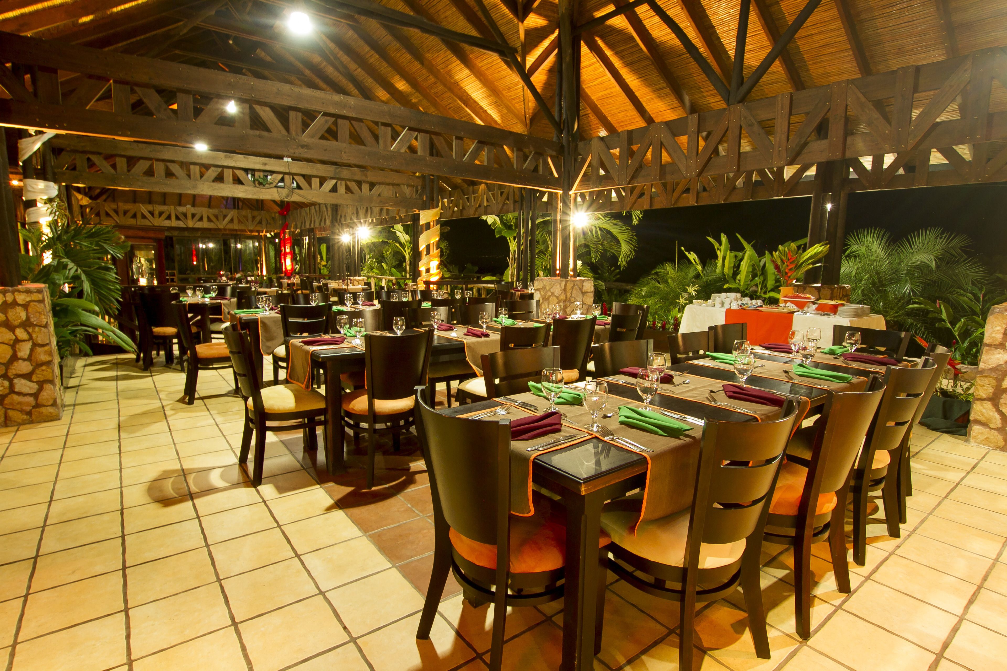 An outdoor restaurant with multiple tables and chairs, a tiled floor, and a wooden ceiling structure.