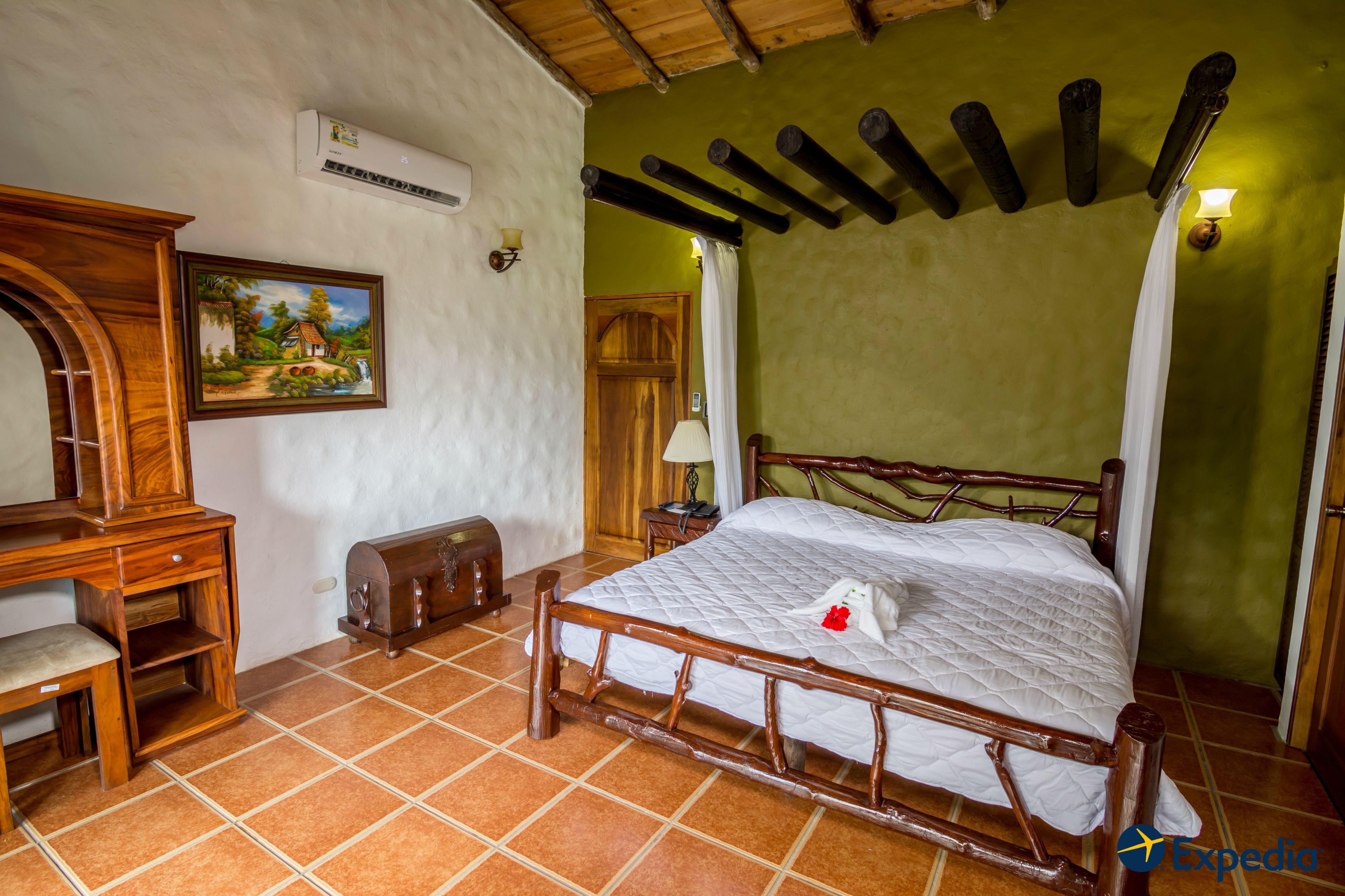Una habitación con una cama de madera, un escritorio con una silla, un cuadro en la pared y un armario de madera.