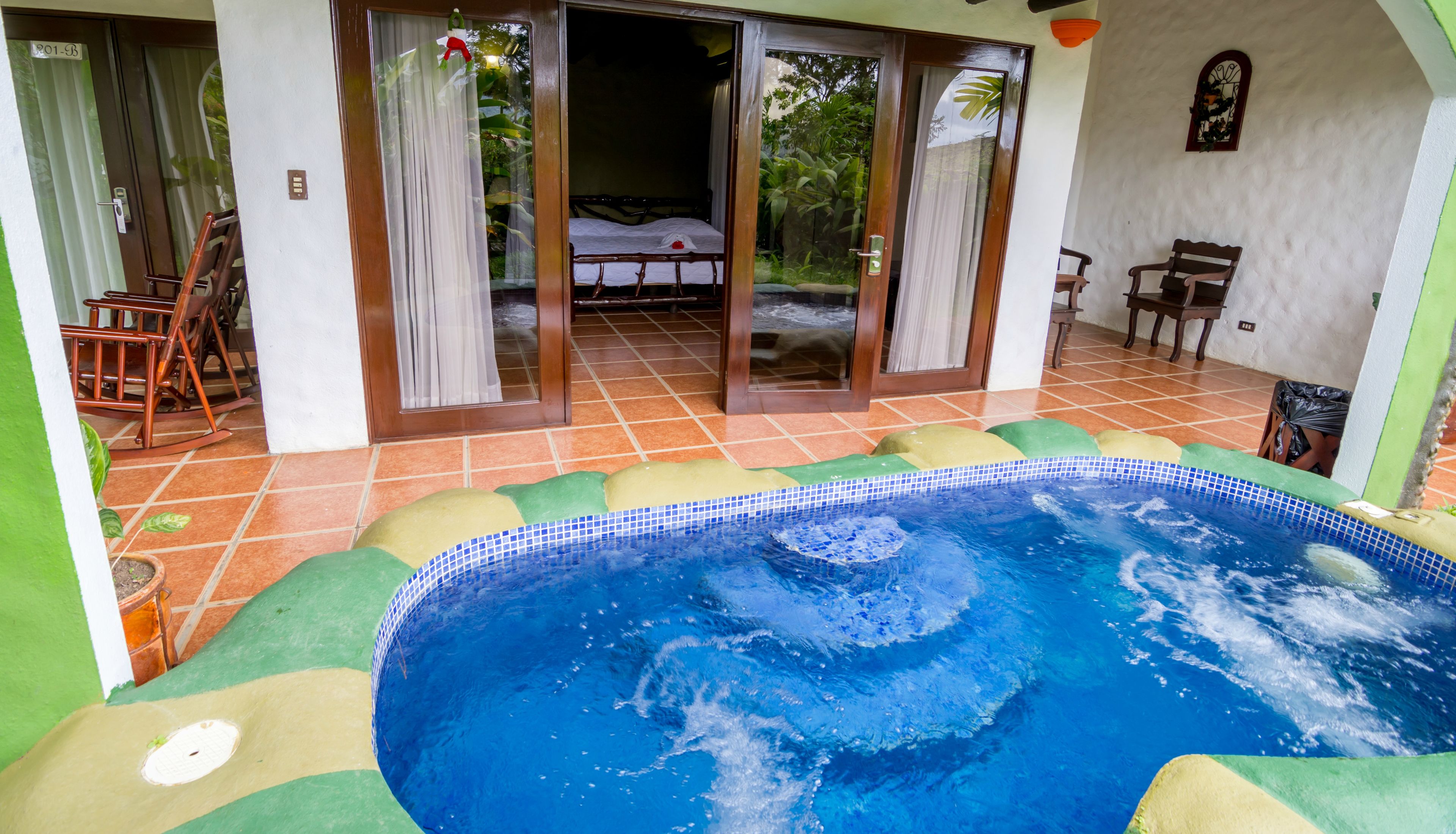 A swimming pool with a tiled deck, a bed with a view, and a dining area with chairs.
