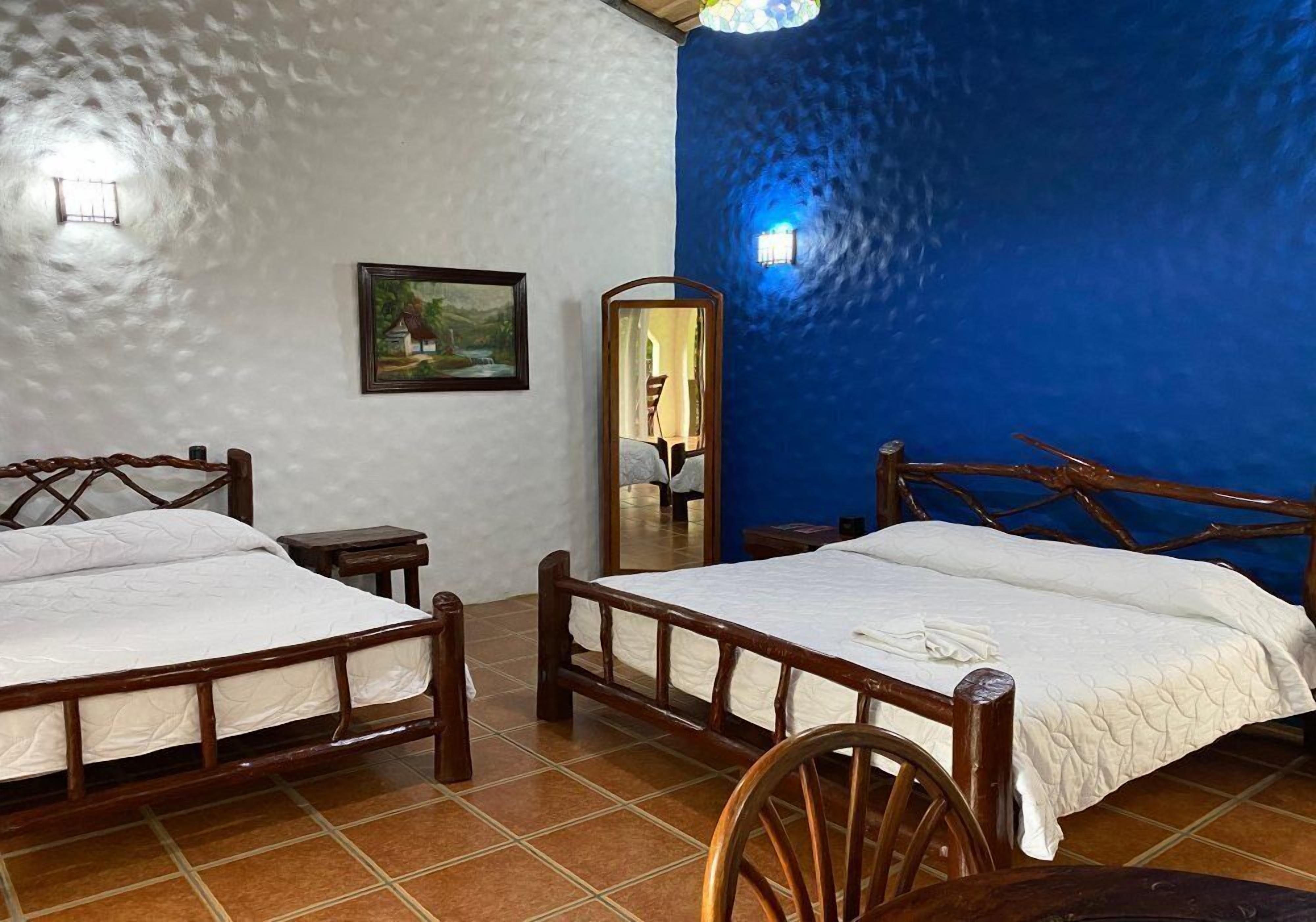 A room with two wooden beds, a small table, a mirror, and a painting on the wall.