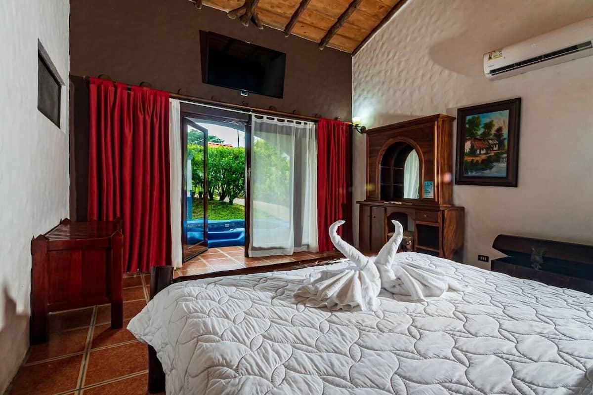 Une chambre d’hôtel avec un lit, une table de chevet en bois, un téléviseur, un tableau et une vue sur la verdure, visible à travers la porte-fenêtre coulissante.