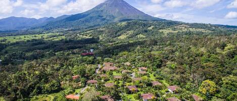 A mountainous landscape with a prominent volcano in the background and a village with houses surrounded by greenery in the foreground.
