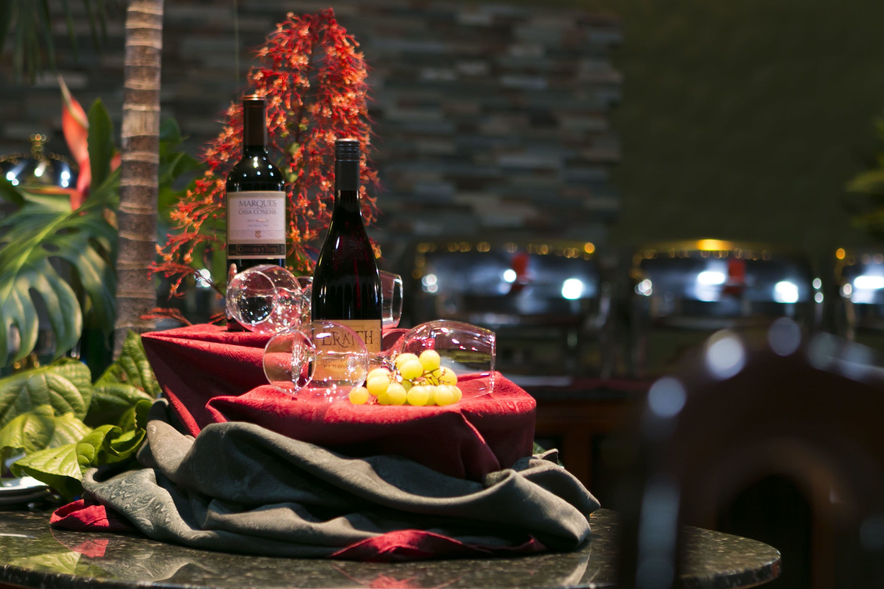 Une table recouverte d’une nappe rouge, une bouteille de vin, un verre et un bol de raisins.