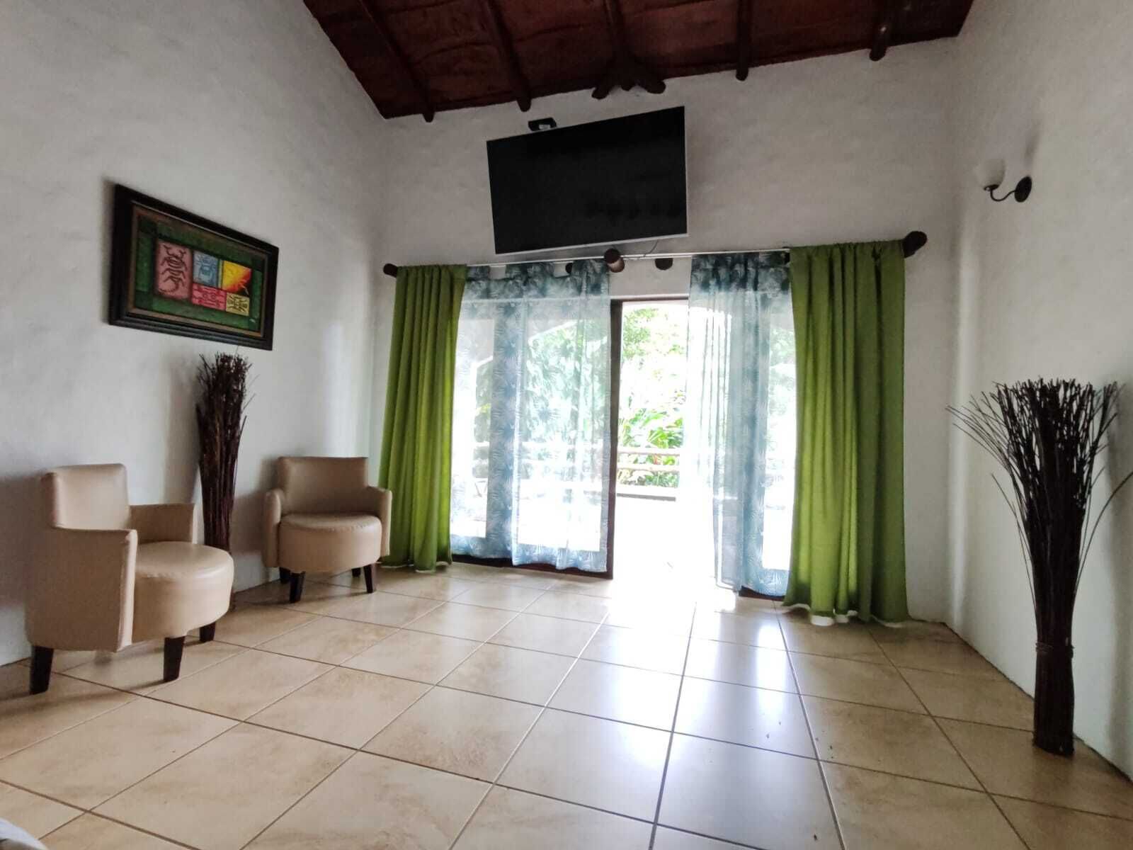 Una habitación amplia con piso de baldosas, dos sillones color beige, una cortina verde y un cuadro enmarcado en la pared.