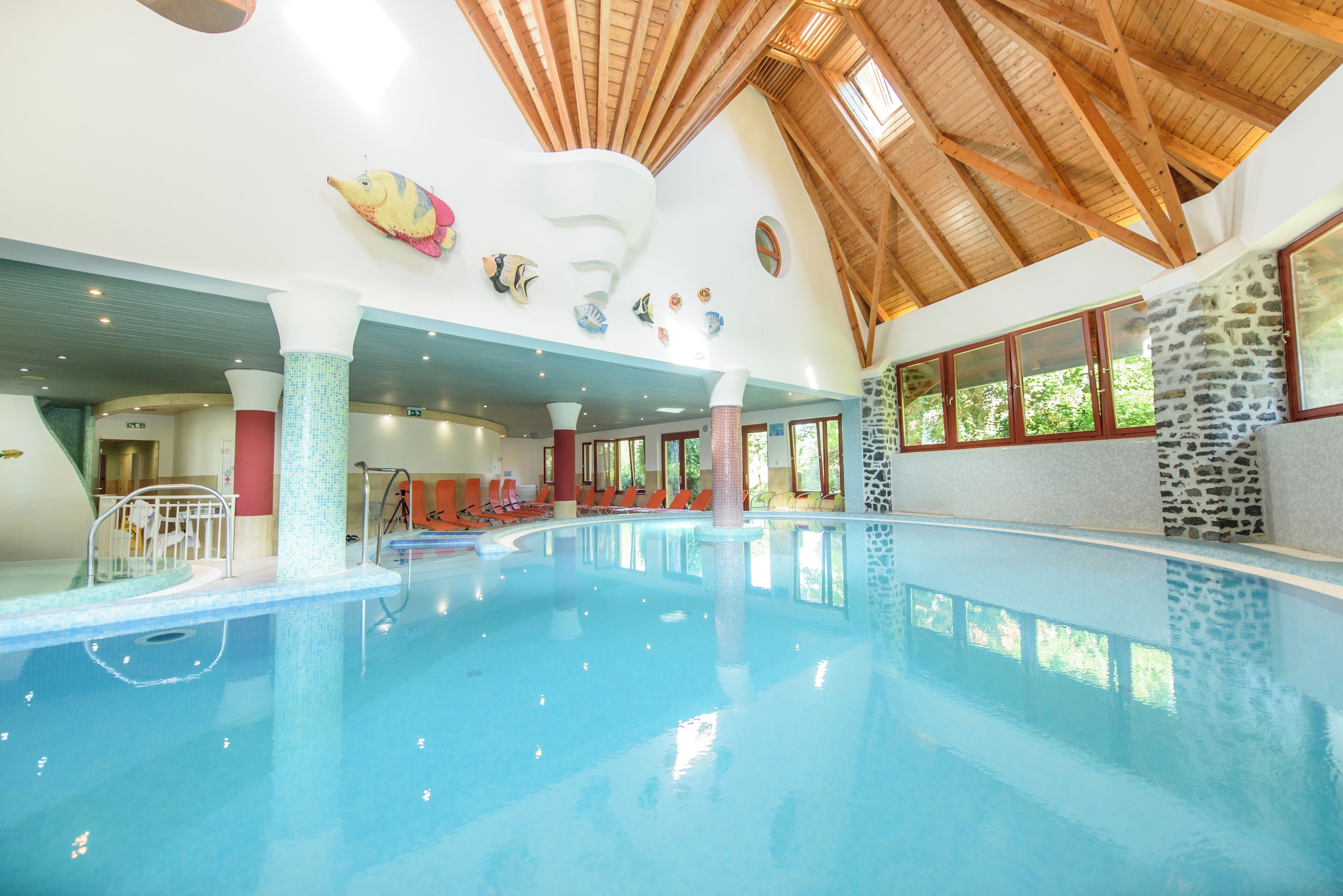 An indoor swimming pool with a high wooden ceiling, stone walls, and colorful wall decorations.