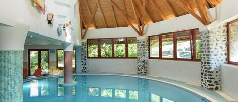 An indoor swimming pool with a high wooden ceiling and stone walls.