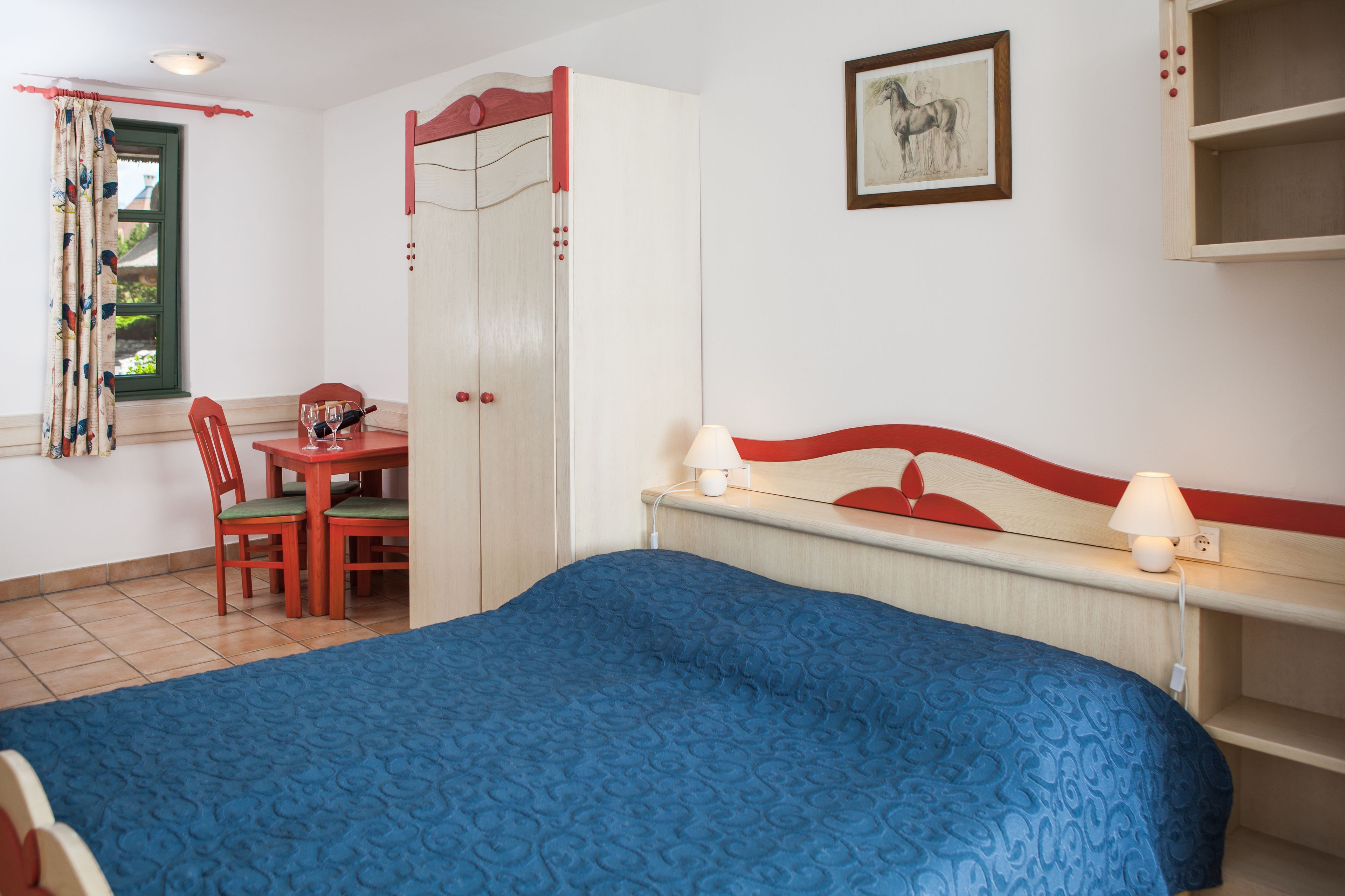 Un dormitorio con cama, escritorio y silla, armario y mesita de noche con lámparas.