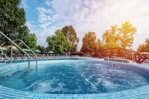Una piscina con sillones de descanso y sombrillas, rodeada de árboles.