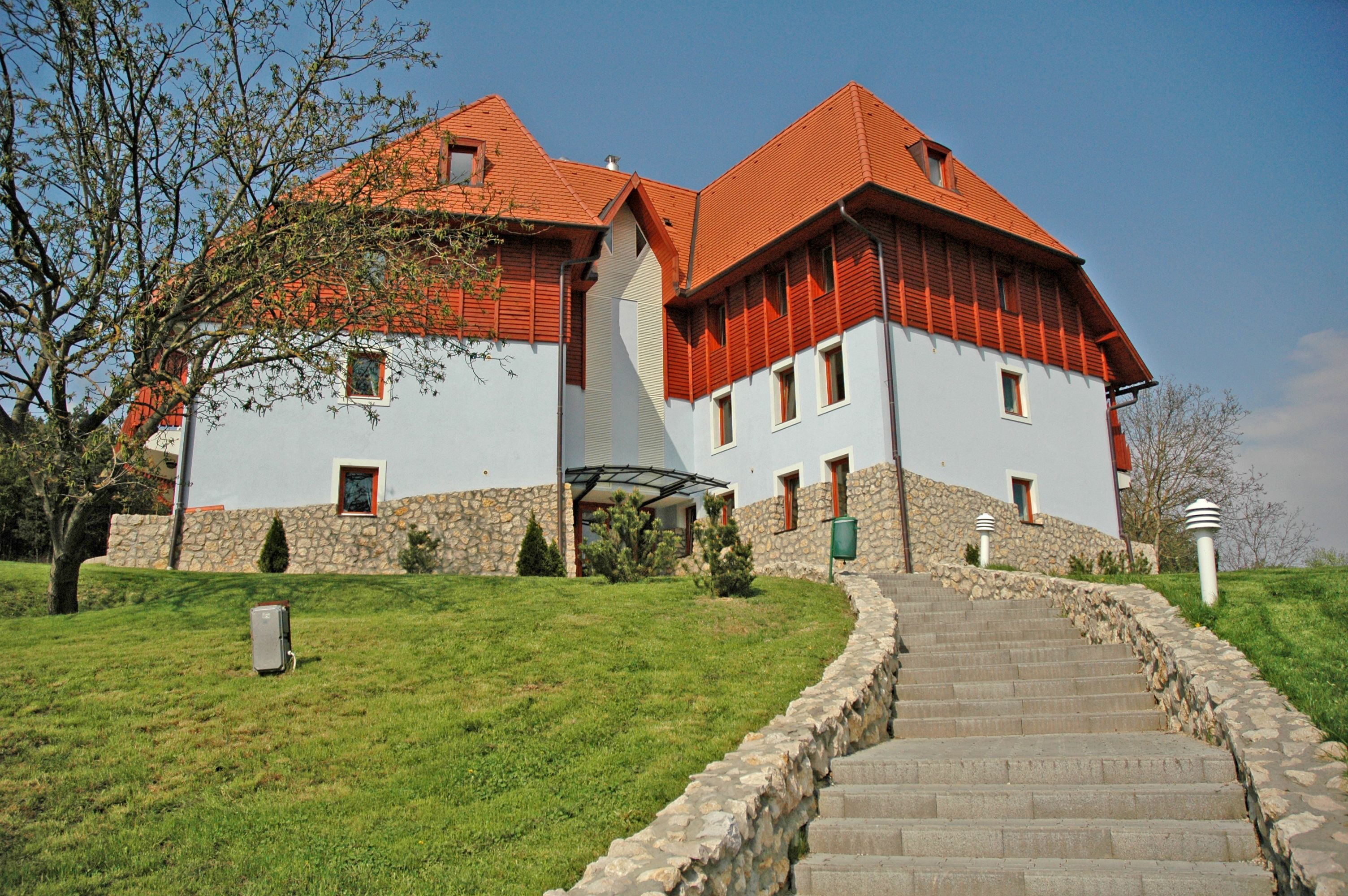 A large building with a stone foundation and red roof, featuring a central staircase leading to the entrance.