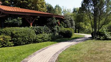 A curved brick pathway leading to a covered pavilion with a red roof, surrounded by lush greenery and trees.