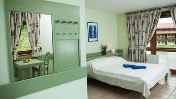 A room with a bed, a table with fruits, a chair, a window with curtains, and a radiator.