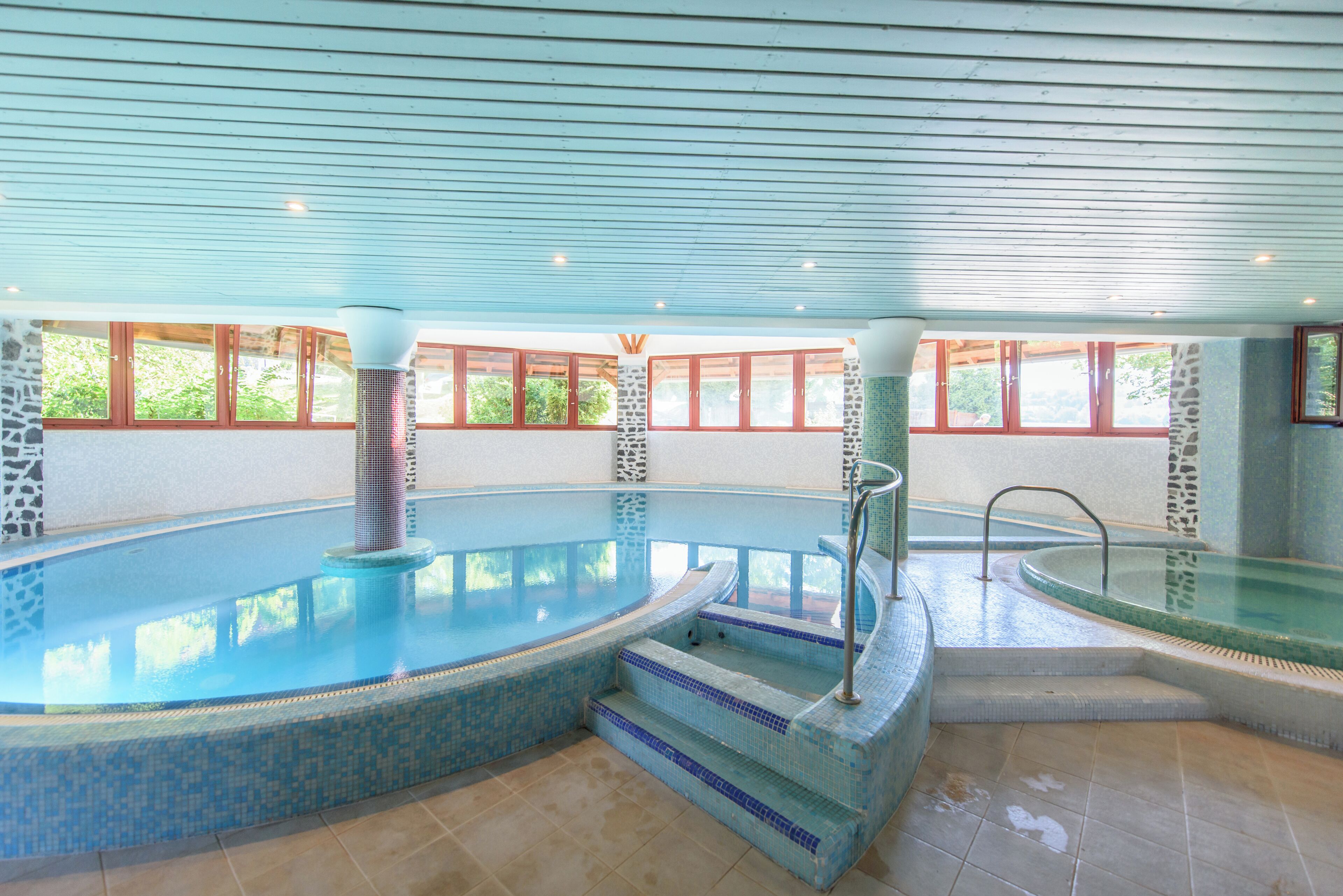 Una amplia piscina interior con agua cristalina, escalones azulejados y una pared de piedra.