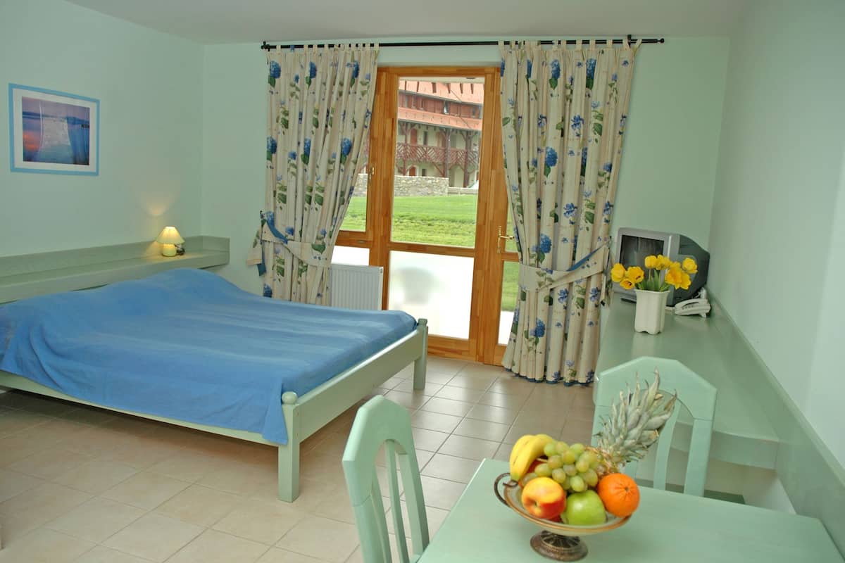 A bedroom with a bed, a table with fruit, and a view of a building through the window.