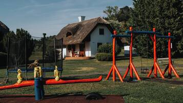 Un parque con una casa de techo de paja, columpios y una estructura roja para hacer ejercicio.