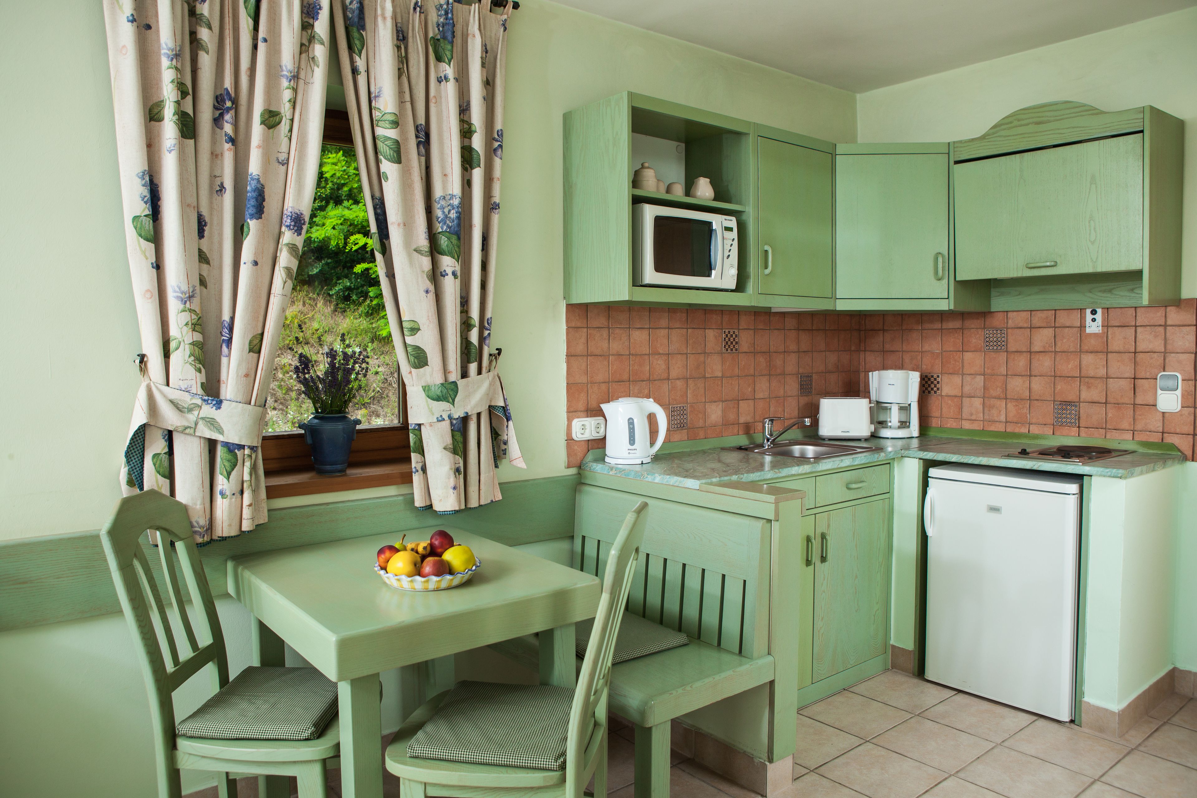 Cocina con decoración verde que incluye una mesa de comedor, sillas, microondas, cafetera y refrigerador.