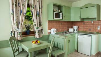 Cocina con decoración verde que incluye una mesa de comedor, sillas, microondas, cafetera y refrigerador.