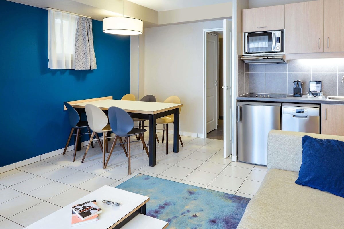 A compact living space with a dining area, kitchenette, and a sofa with a blue pillow.