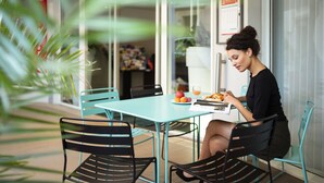 A woman sitting at a table with a plate of food and a drink, in a room with a glass door and a calendar on the wall. - Aparthotel Adagio Monaco Monte Cristo (Beausoleil)