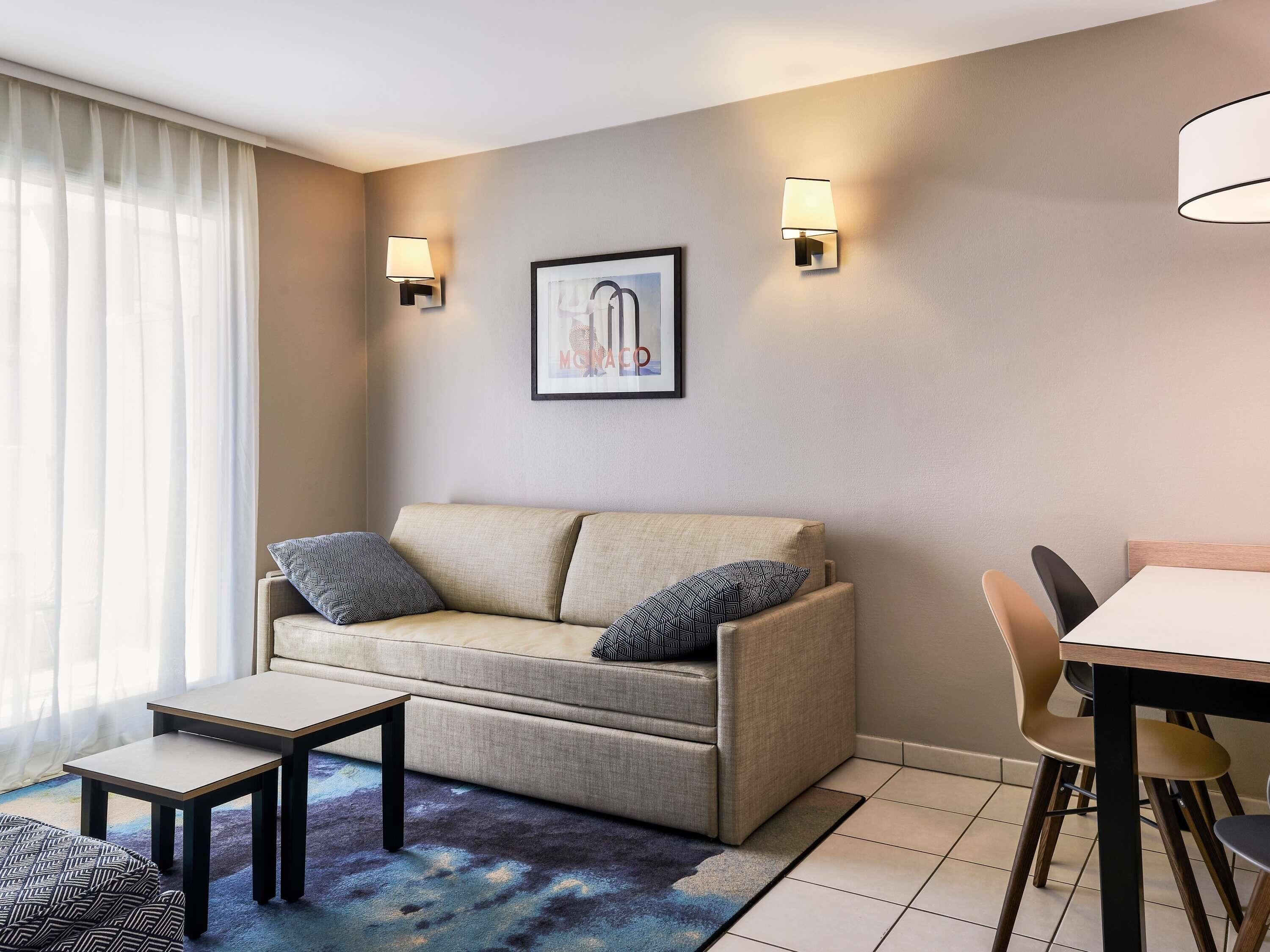 Una sala moderna con un sofá, dos mesas auxiliares, una mesa de comedor con sillas y un cuadro en la pared.