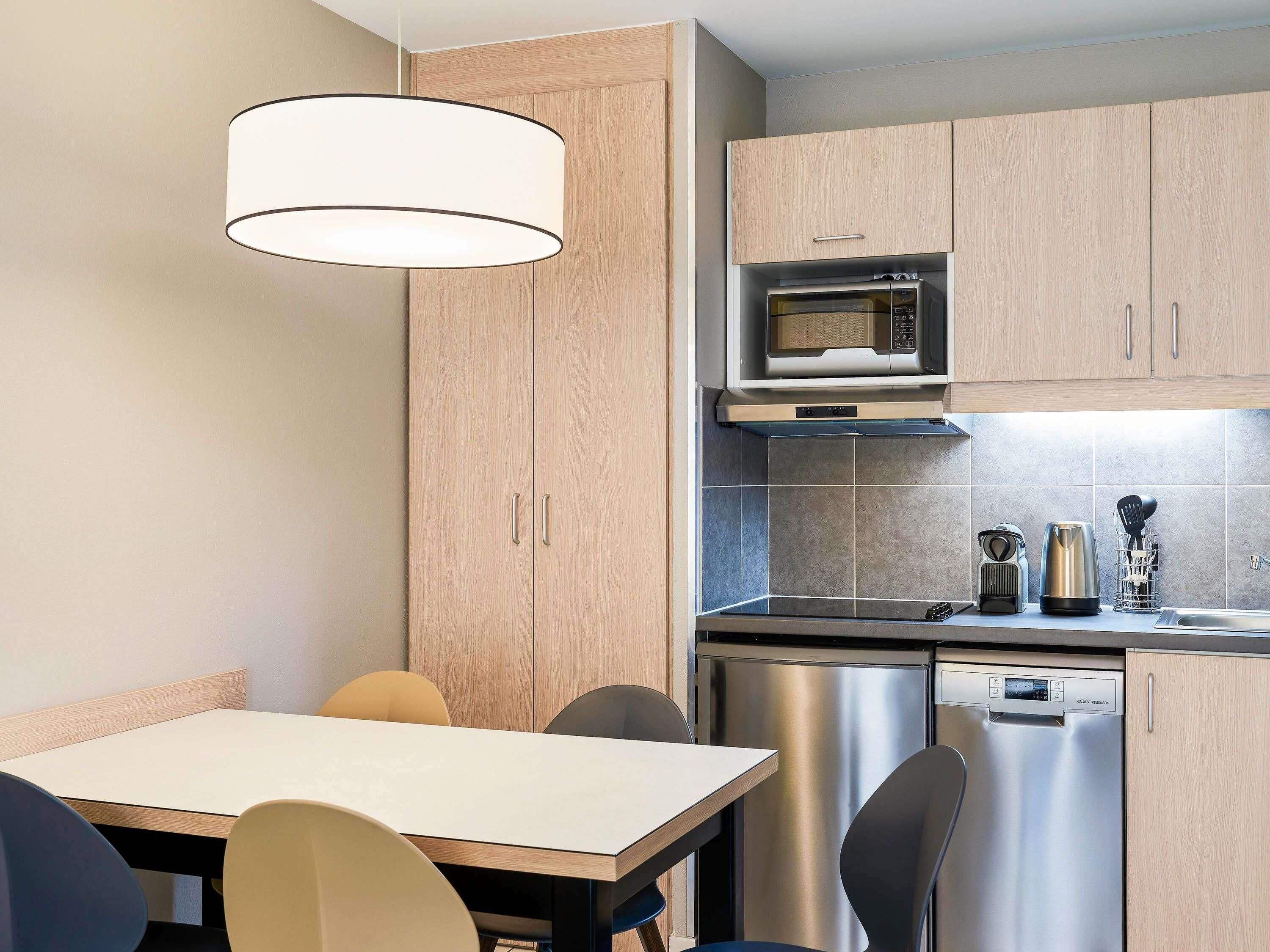 A modern kitchen with wooden cabinets, a microwave, a dishwasher, and a dining area with a table and chairs.