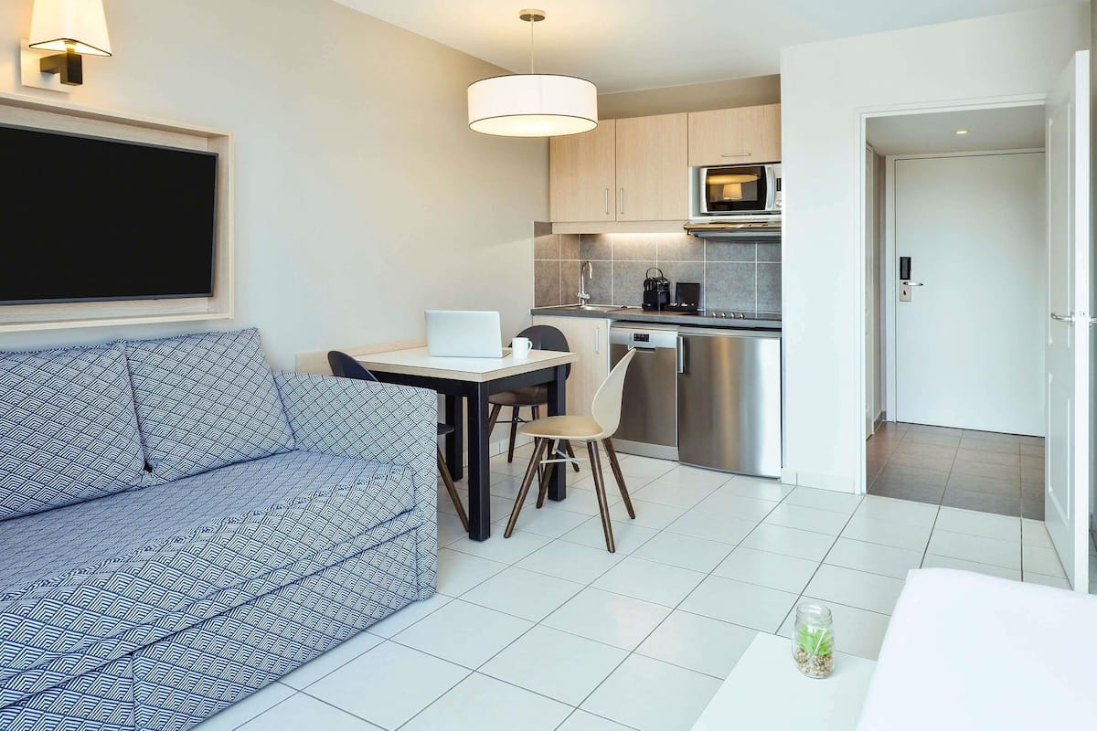 A modern kitchen with a microwave, dishwasher, and a dining area with a laptop and a coffee cup.
