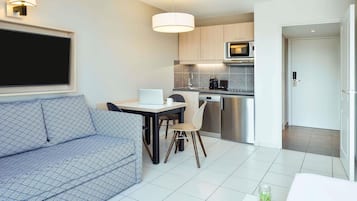 A modern kitchen with a microwave, dishwasher, and a dining area with a laptop and a coffee cup.