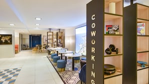A modern coworking space with tables, chairs, and a large screen. - Aparthotel Adagio Monaco Monte Cristo (Beausoleil)