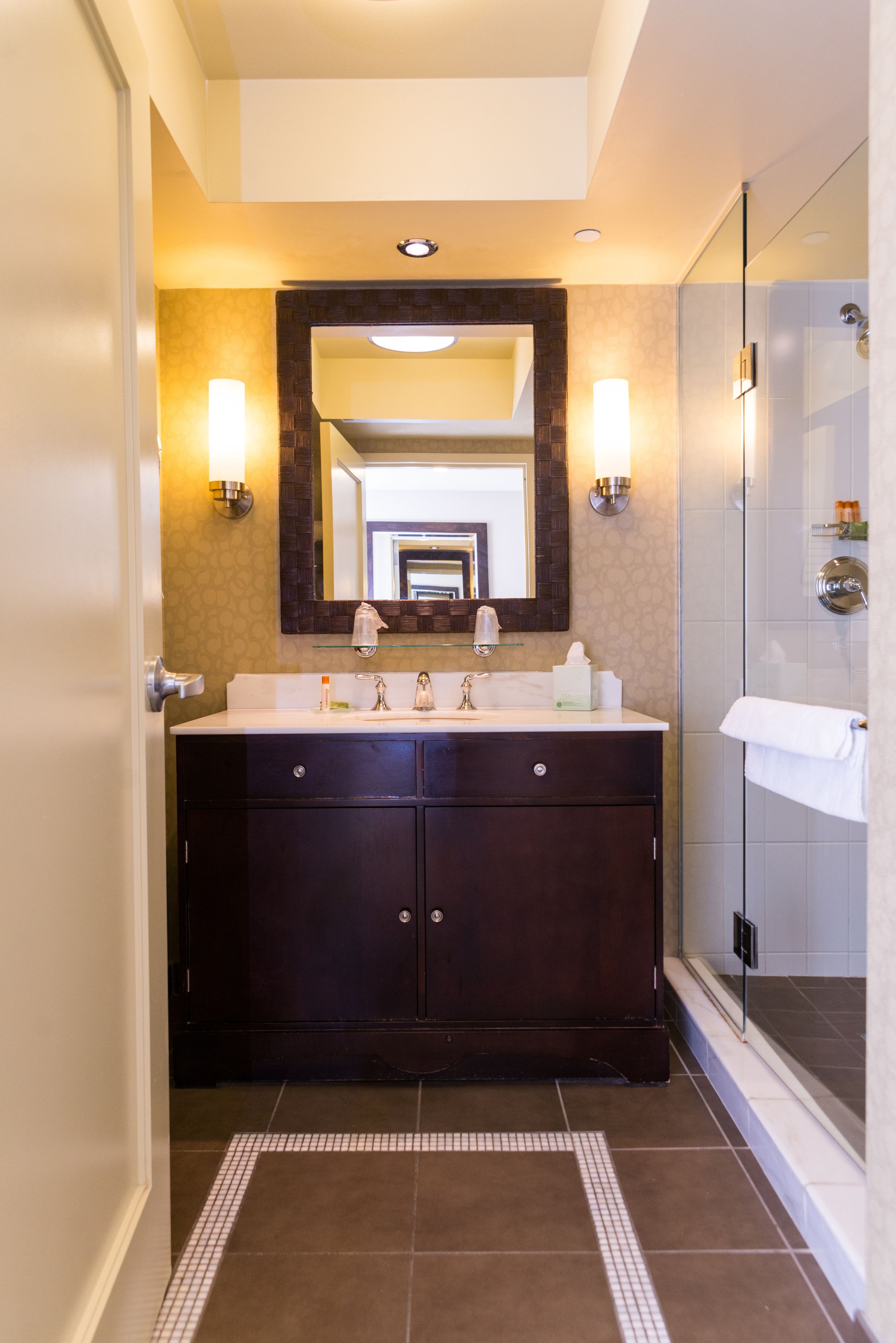 A modern bathroom with a dark wooden vanity, a large mirror, and a glass shower enclosure.