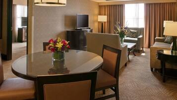 A hotel room with a round dining table, two armchairs, a sofa, a TV, and a lamp.