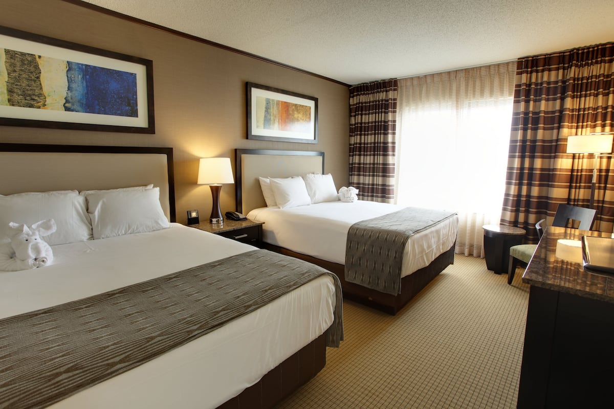 A hotel room with two beds, a desk, a chair, and a lamp.