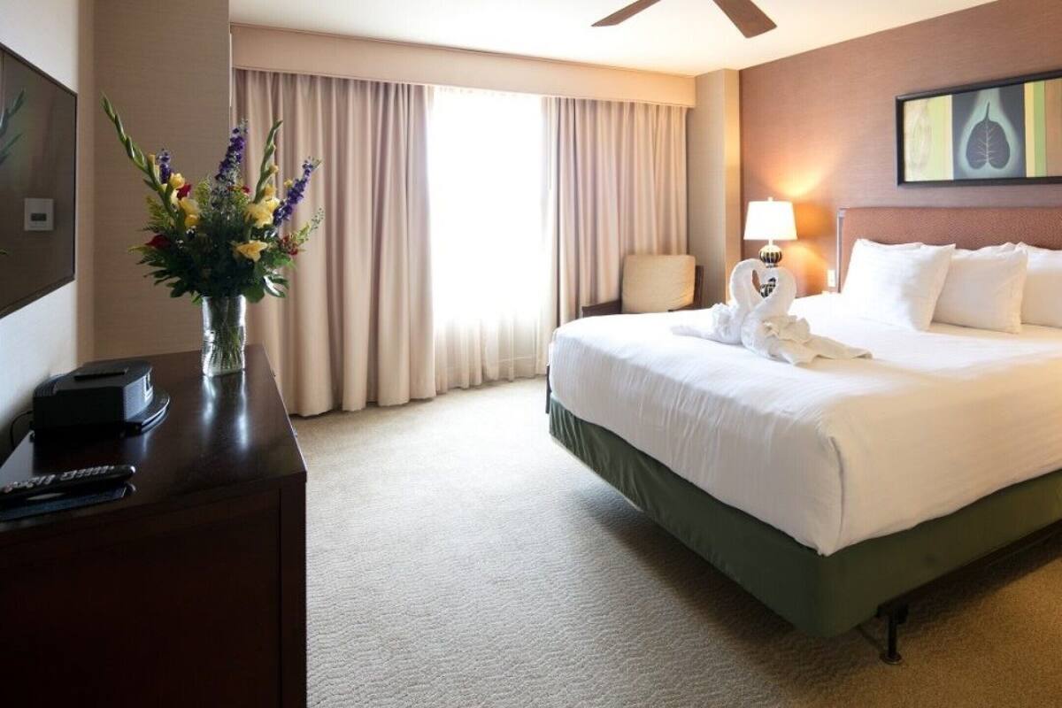A hotel room with a large bed, a desk with a lamp, a vase with flowers, and a painting on the wall.