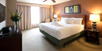 A hotel room with a large bed, a desk with a lamp, a vase with flowers, and a painting on the wall.