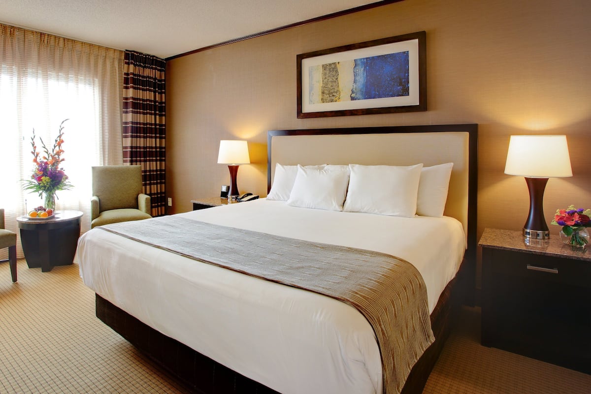 A hotel room with a large bed, two bedside lamps, a chair, a small table with a vase of flowers, and a framed picture on the wall.