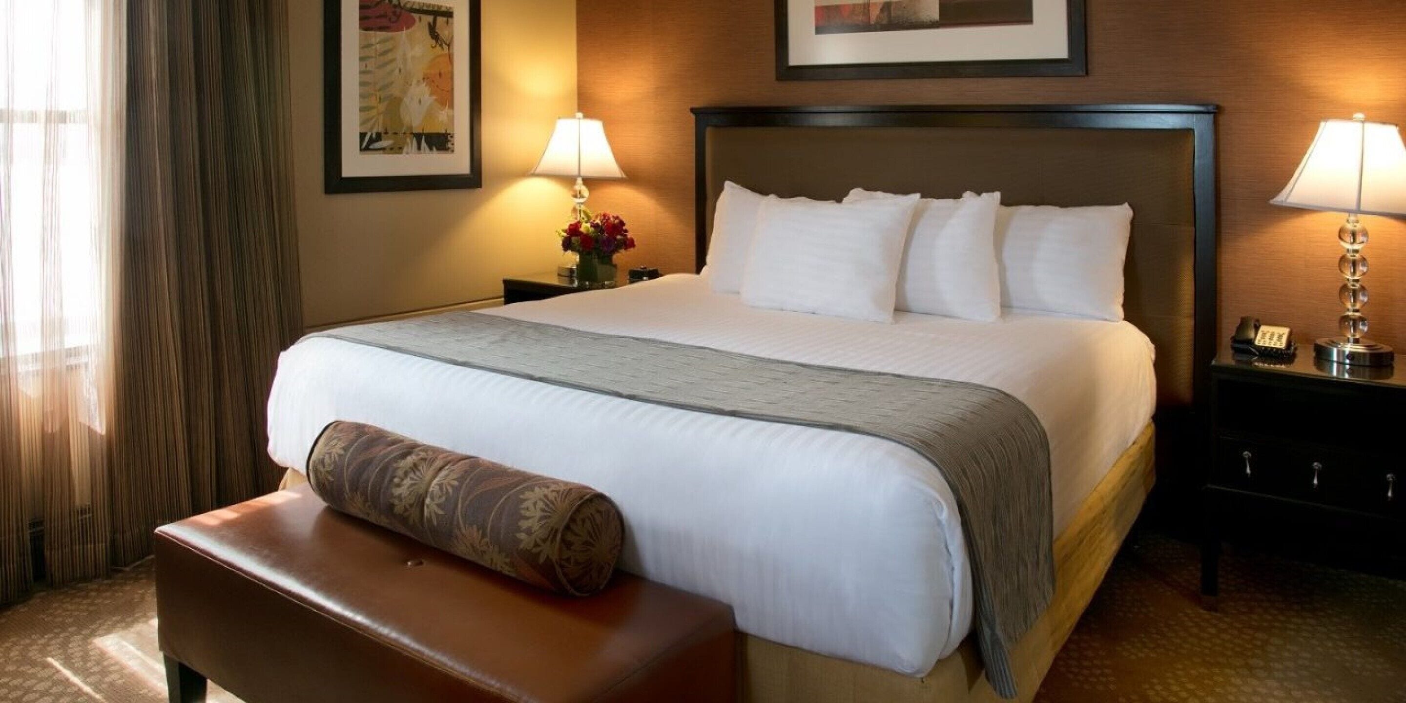 A hotel room with a large bed, two bedside lamps, a nightstand with a phone, and a window with curtains.