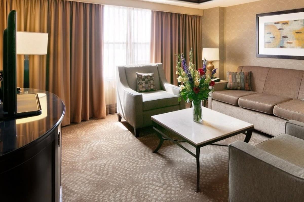 A hotel room with a sofa, armchairs, a coffee table, a TV, and a painting on the wall.